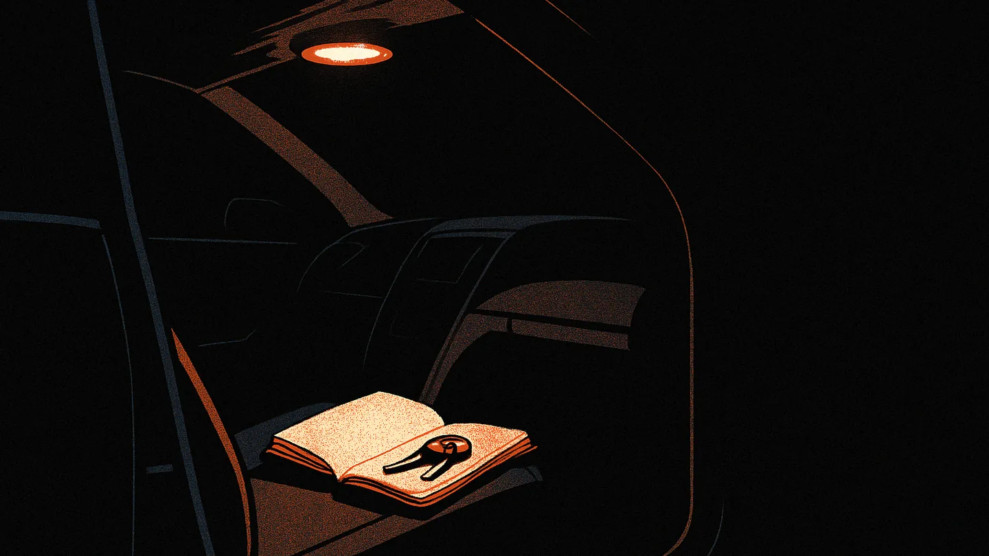 A notebook and keys on a car seat, lit by a single warm dome light, the rest of the interior dark.