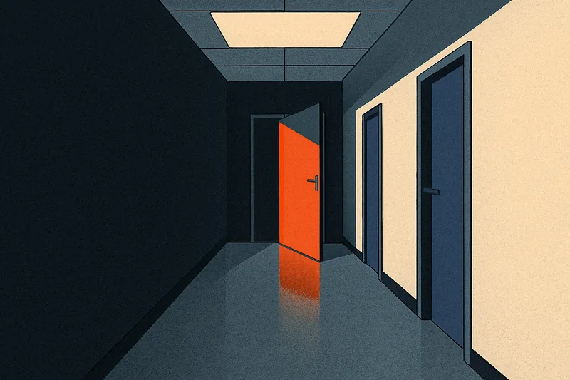 An empty office corridor leading toward a half-open door glowing warm orange at the far end.